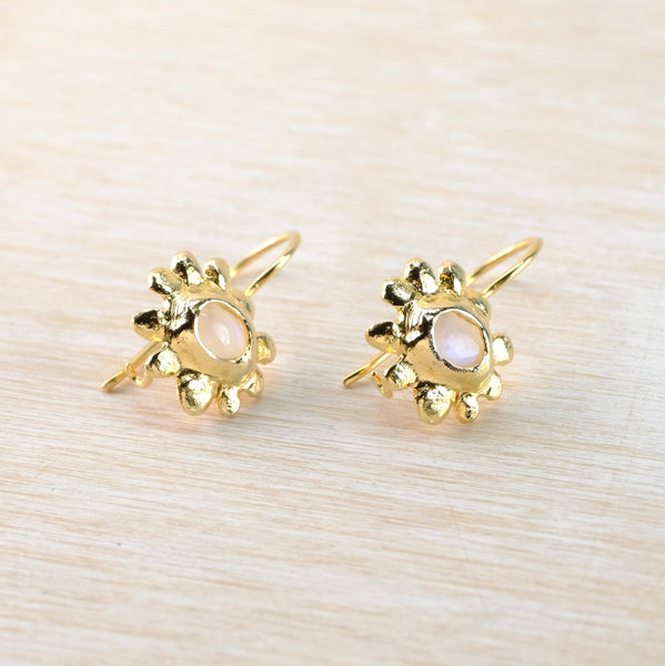 Gold earrings with a central gemstone on a light wood background