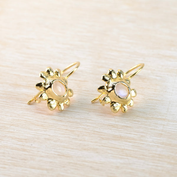 Gold earrings with a central gemstone on a light wood background