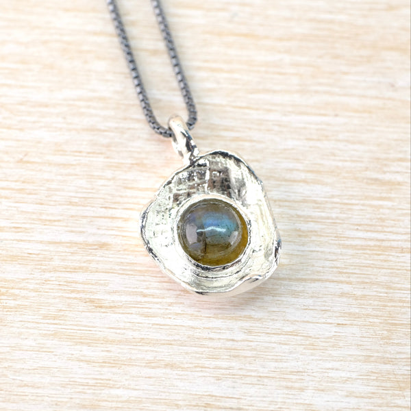 Silver pendant with a central gemstone on a light wood surface