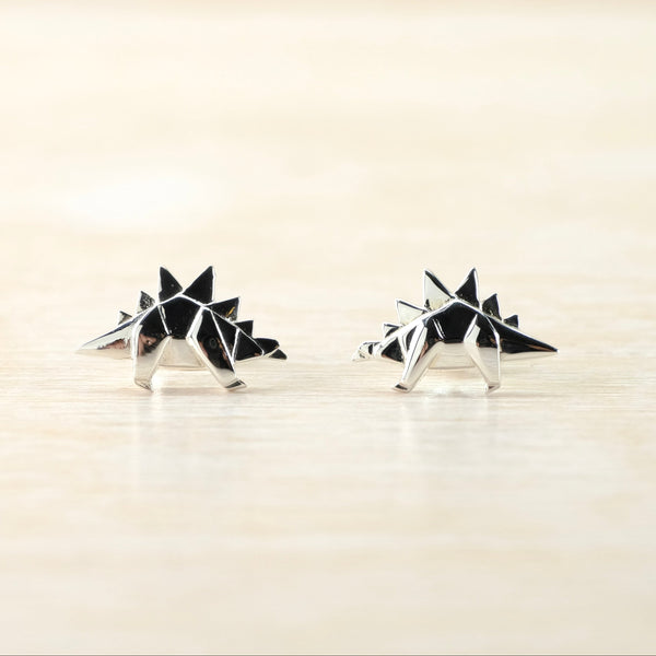 Pair of geometric dinosaur stud earrings on a light background