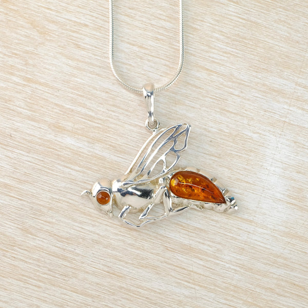 Silver fly pendant with amber accents on a light wood background