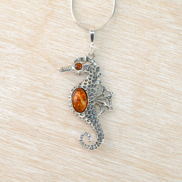 Silver seahorse pendant with amber stones on a beige background