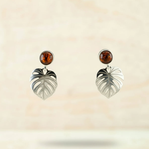 Silver earrings with leaf design and amber stones against a beige background