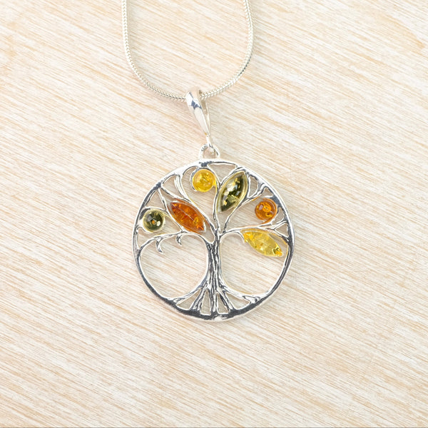 Tree-shaped pendant with colored  amber stones on a silver chain against a beige background
