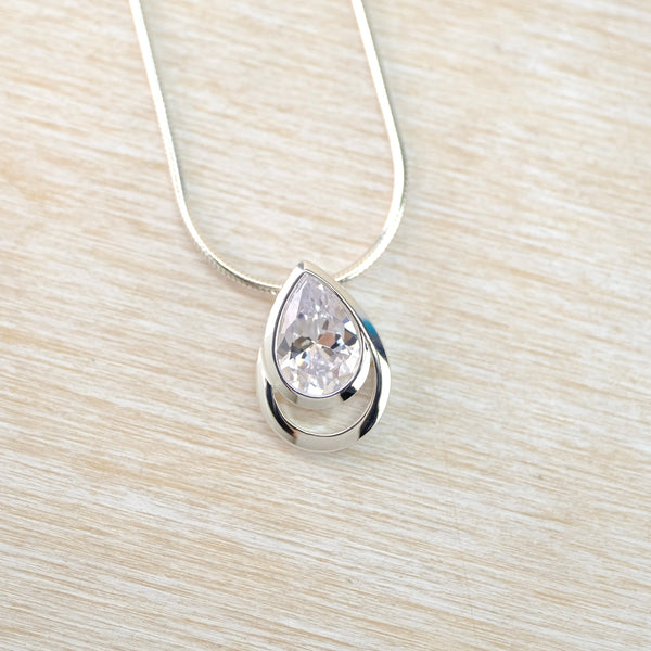 Teardrop-shaped crystal pendant on a silver chain against a light wood background