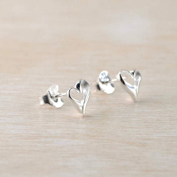 Silver heart-shaped stud earrings on a light wood background