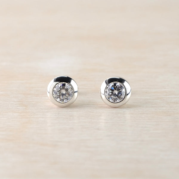 Pair of silver stud earrings with clear gemstones on a light beige background