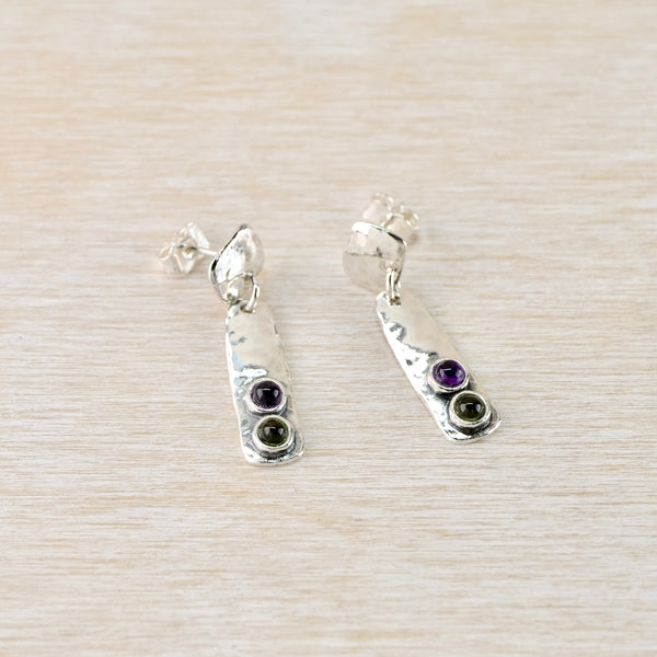 Silver earrings with gemstones on a light wooden surface