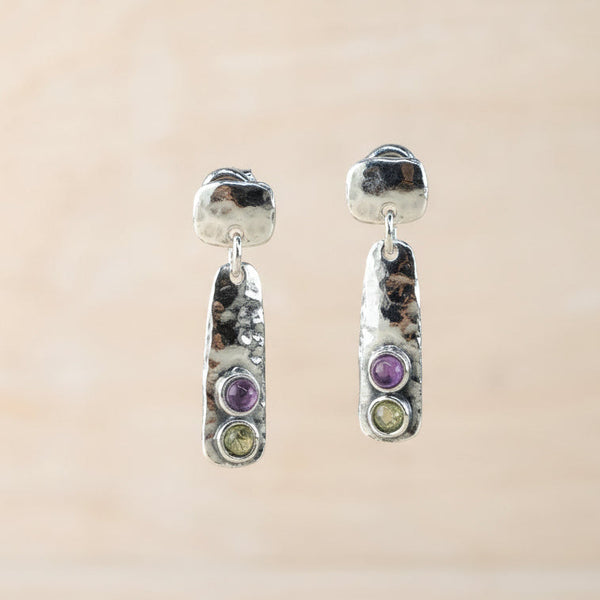 Pair of earrings with gemstones on a stand against a beige background