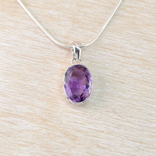 Amethyst pendant on a silver chain against a light wood background