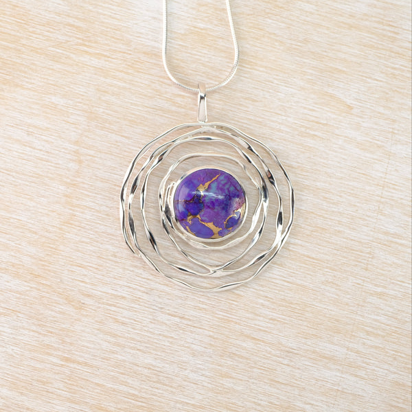 Silver pendant with a purple gemstone on a wooden surface