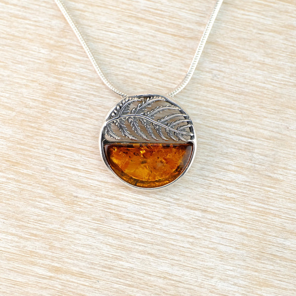 Circular Silver pendant with amber stone on a light wood surface