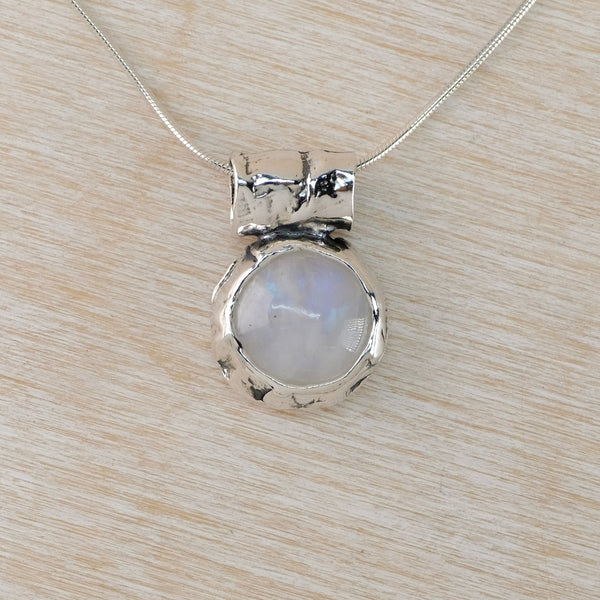 Silver pendant with a milky pale blue stone on a light wood surface