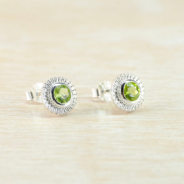 Pair of silver earrings with green gemstones on a beige background