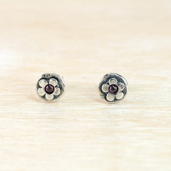 Round earrings with a flower motif and red garnet stones on a beige background