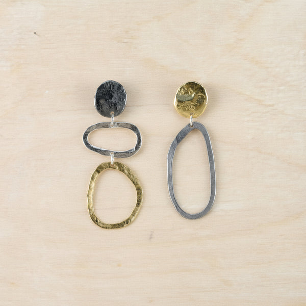 Pair of  dangly asymmetric earrings against a beige background