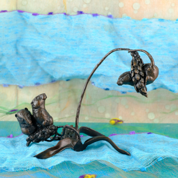 A dark  bronze sculpture of three mice on a curved wheat stem, displayed on a textured blue fabric surface.