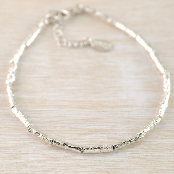 16 fine slender cylindrial beads are threaded in a circle to go around the wrist, They are all finely textured with a hammered finish to prettily catch the light.