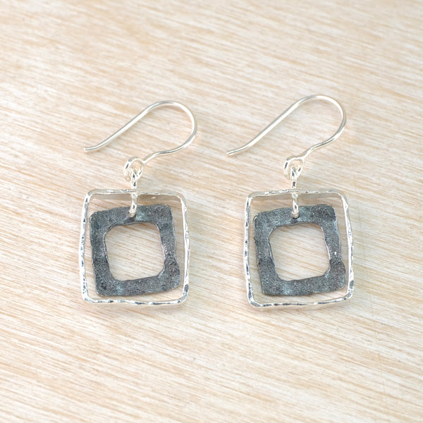 Dangly earrings formed of an open hammered and oxidised square suspended from and framed by another square of hammered bright silver. 