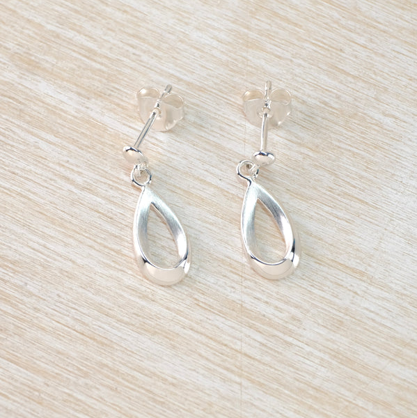 Silver open teardrop earrings on a light wood surface