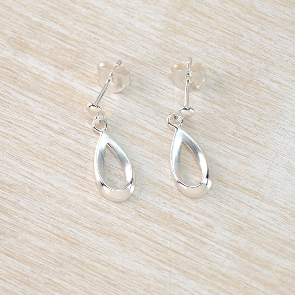 Silver open teardrop earrings on a light wood surface
