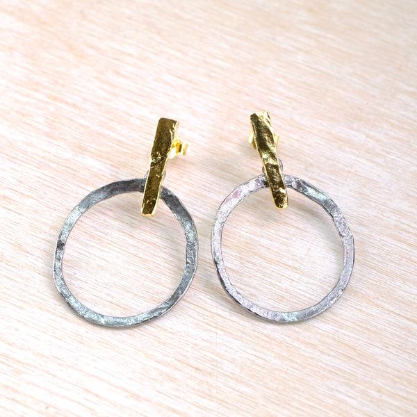 Pair of hoop earrings with gold and silver finishes on a light wood surface