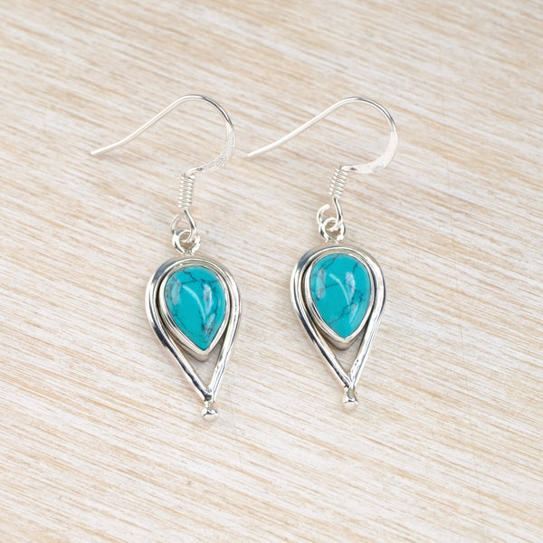 Turquoise teardrop earrings with silver frames on a light wood surface