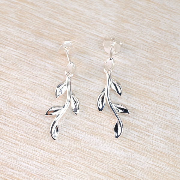 Silver twig with four leaves  earrings on a light wood surface