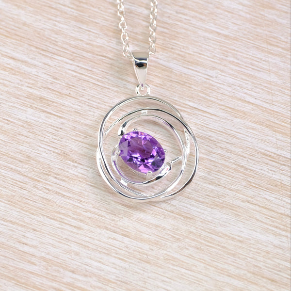 Silver pendant with a purple gemstone in a spirally wire-work setting.