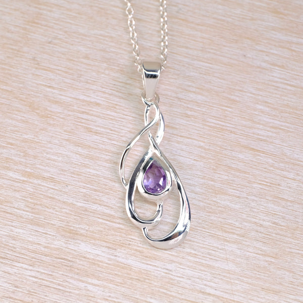 Silver pendant with a purple gemstone on a light wood background
