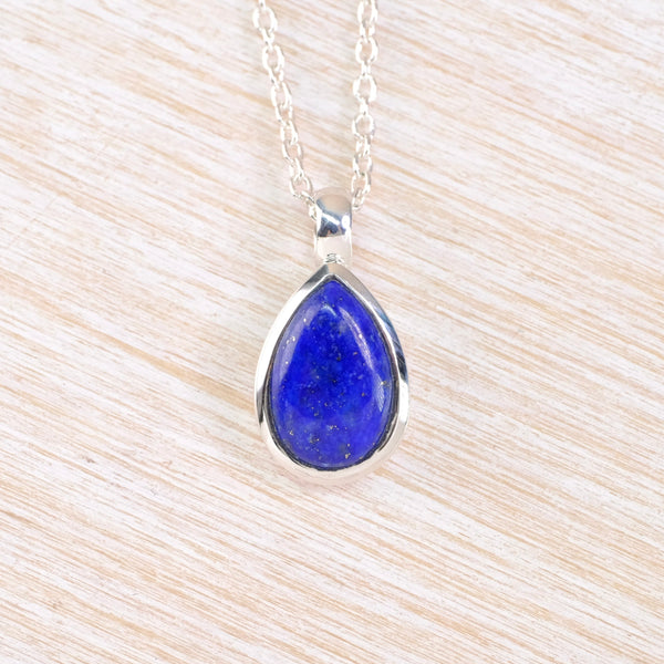 Teardrop-shaped  navy blue pendant on a silver chain against a beige background