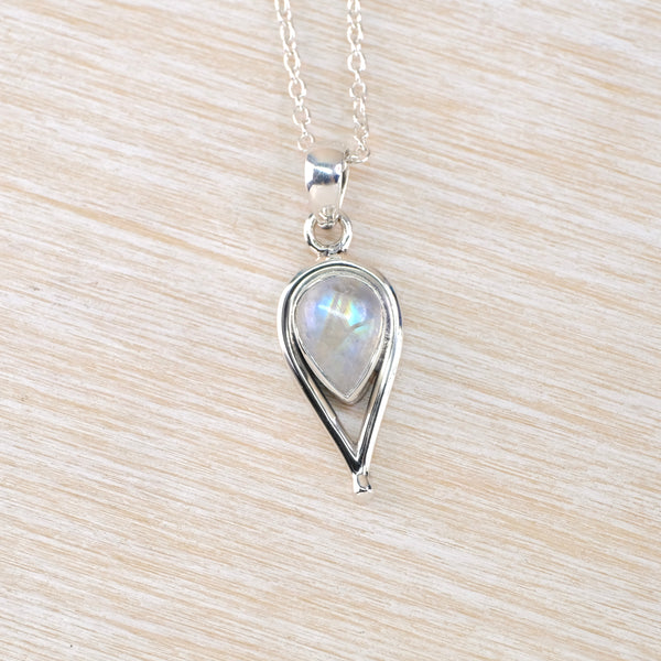 Silver teardrop pendant with a rainbow moonstone on a light wood background