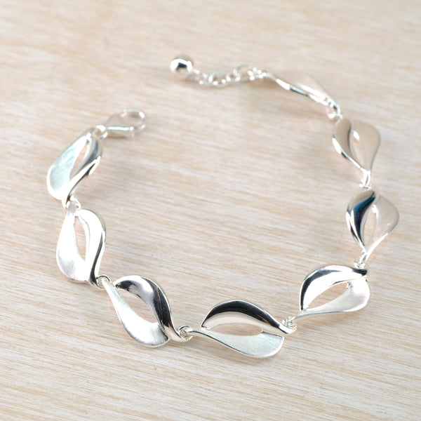 Silver bracelet with leaf-like links on a light wood surface