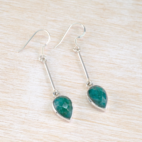 Teal heart-shaped gemstone earrings on silver hooks on a light wood background