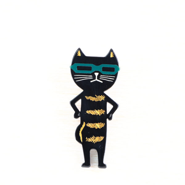 Black cat-shaped brooch with gold stripes and teal sunglasses in a cartoon style.