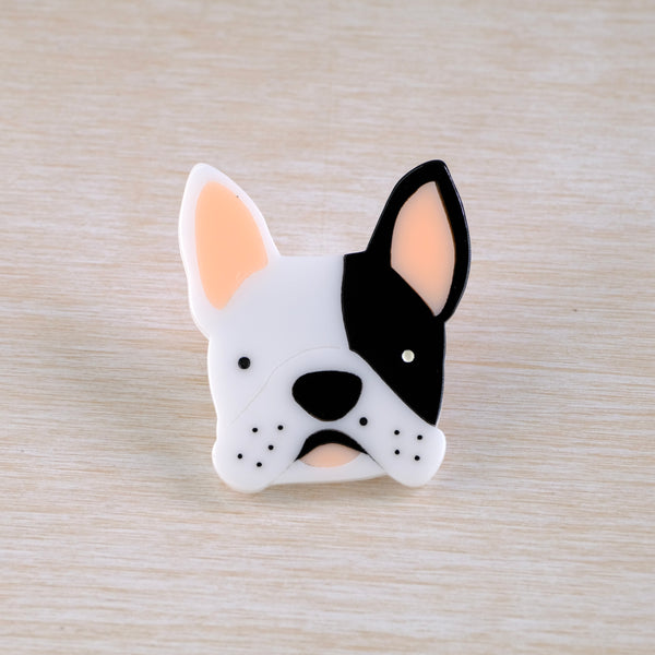 A resin brooch in the shape of the face of a French Bulldog, in white, black and peach tones.