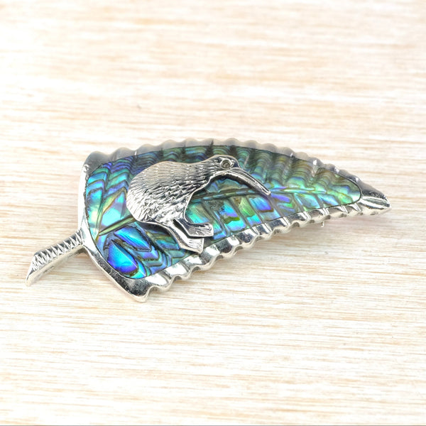 Decorative  brooch with abalone shell and a bird design on a textured beige background