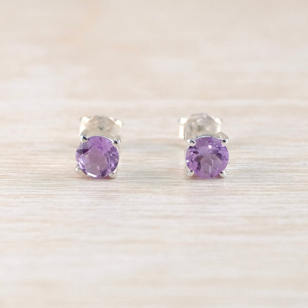 Pair of silver stud earrings with purple gemstones on a light wooden surface