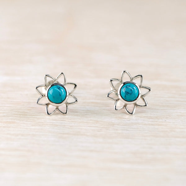 Pair of flower shaped silver earrings with turquoise stones on a light wooden background