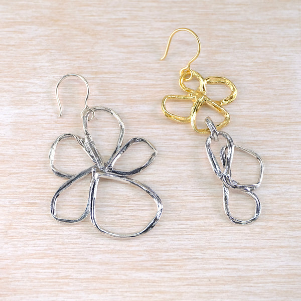 Pair of silver and gold earrings with flower outline designs, each earring being different in form