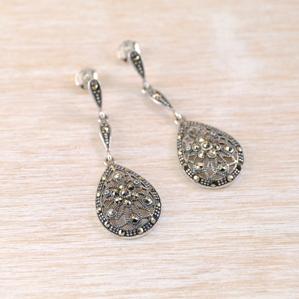 Pair of silver teardrop earrings with intricate designs on a light wood surface
