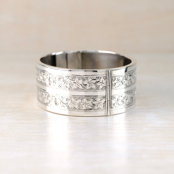 A silver bangle bracelet with fine engraving of leaves all around its sides.
