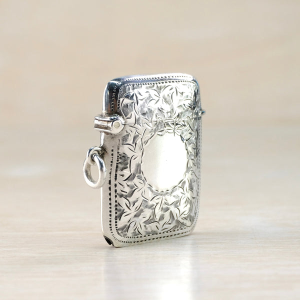 Silver engraved vesta case with hinged top on a light beige background