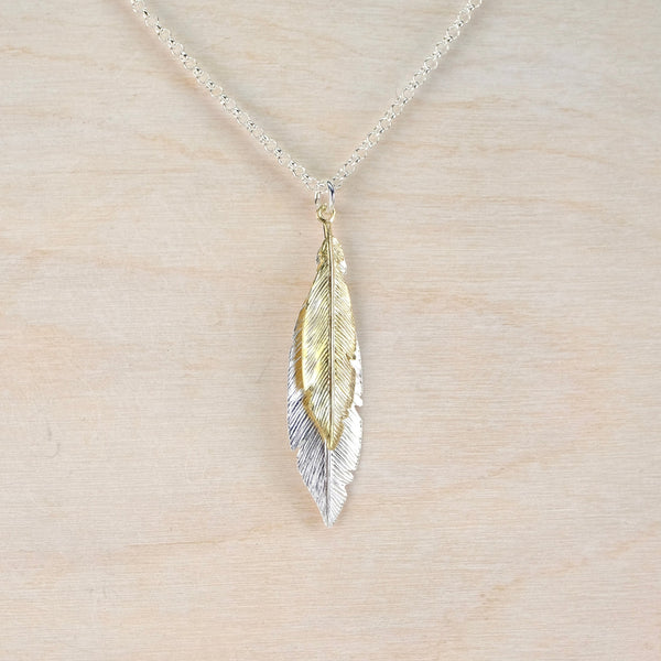 Necklace with a  double feather-shaped pendant on a light wood background