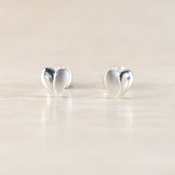 Heart-shaped silver earrings on a reflective surface with a light background