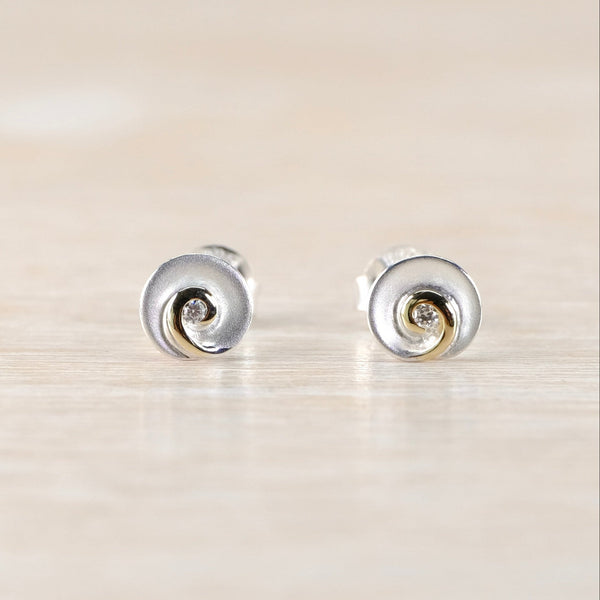 Pair of silver earrings with a small diamond and a swirl design on a beige background