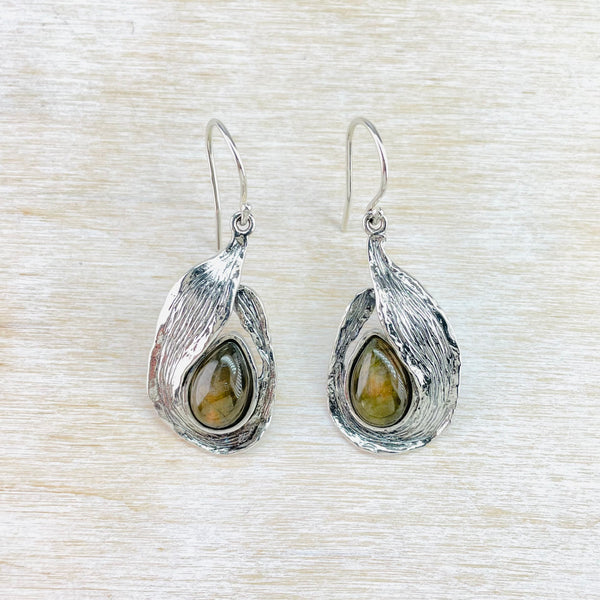 A pair of silver teardrop-shaped earrings with labradorite gemstones set in them, displayed on a white textured background.