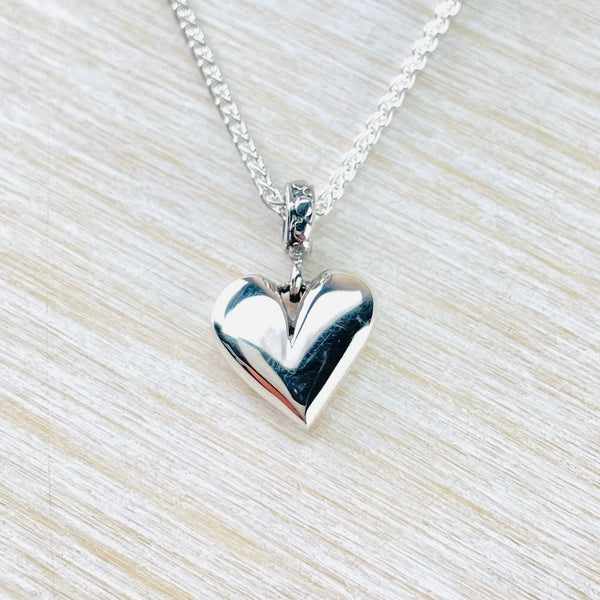 Silver heart-shaped pendant on a chain against a light wood background