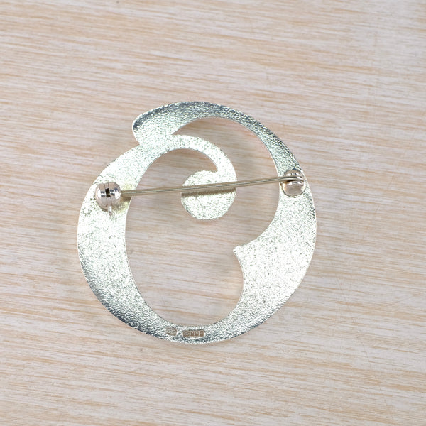Silver brooch with circular design on a wooden surface