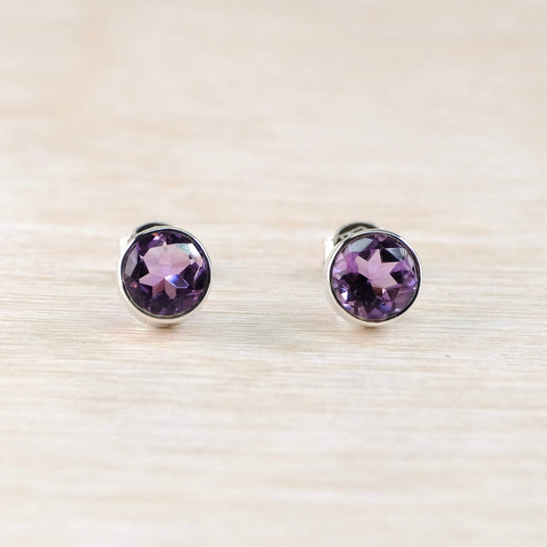 Pair of purple gemstone stud earrings on a light wood background